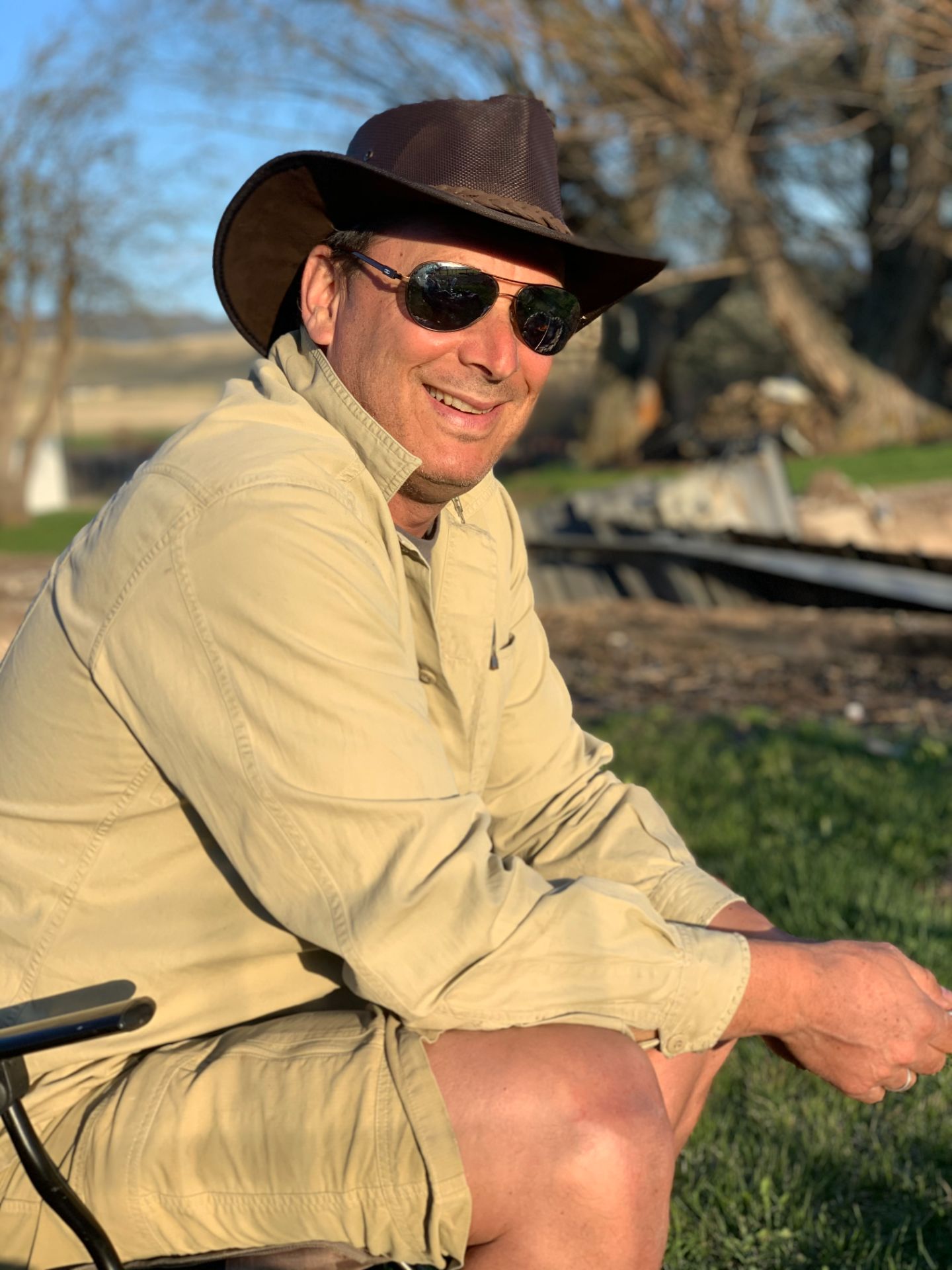 Man sitting in a chair wearing a brown hat and sunglasses.